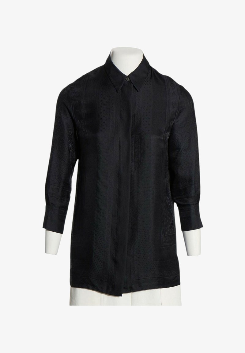 Chemise noire à manches longues avec un motif subtil, col classique et boutons avant cachés sur un buste de mannequin blanc.