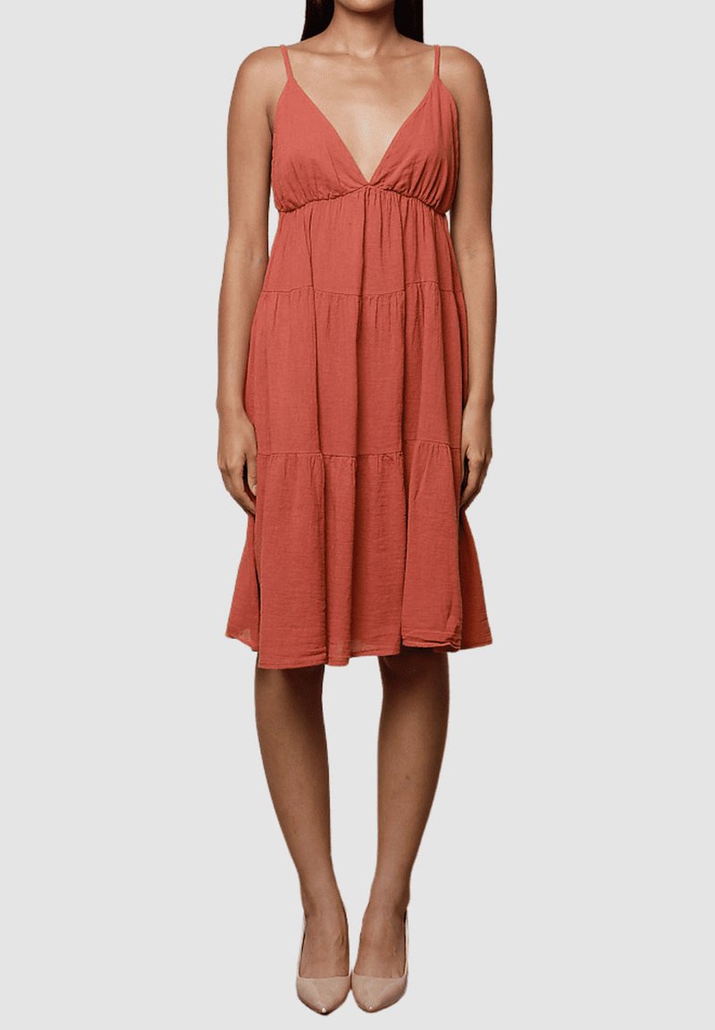 Vestido sin mangas de color óxido con un profundo escote en forma de V, diseño de capas y una tela texturizada ligera. De longitud media con una silueta fluida.