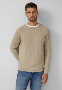 Beiger Pullover mit langen Ärmeln, rundem Ausschnitt und weißem Rand. Weiche Textur, figurbetontes Design, kombiniert mit blauen Jeans.