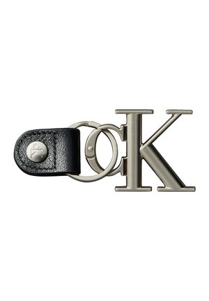 Llavero de metal con correa de cuero negra y botón plateado, con grandes letras pulidas "C" y "K" conectadas por un anillo metálico.