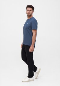 Dunkelblaues kurzärmliges T-Shirt mit Rundhalsausschnitt und kleinem weißen Logo. Getragen mit schwarzen Slim-Fit-Jeans und weißen Sneakers.