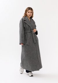 Lungo cappotto in lana grigia con un ampio colletto, vita con cintura e vestibilità ampia. Presenta maniche larghe e una finitura morbida e testurizzata.