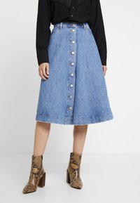 Jeanskjol i midi-längd i ljusblått med utsvängd form, knappstängning fram och fransig fåll; bärs med mönstrade ankelboots.