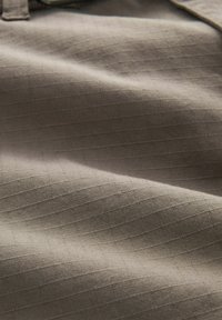 Beige tyg med en subtil rutad struktur, som visar släta kurvor och mjuka veck. Materialet verkar lätt och andningsbart.