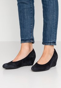 Scarpe con tacco a cuneo in suede nero, con punta arrotondata e design a scollo basso, abbinate a jeans blu slim fit.