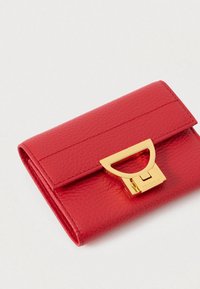 Červená texturovaná kožená peněženka s obdélníkovým límcem a zlatým kovovým zapínáním na jednotném pozadí.