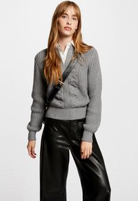 Pull en tricot gris avec un col en V profond et des poignets côtelés, associé à un pantalon large en cuir noir. Comprend un sac à bandoulière élégant.