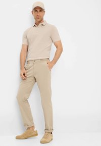 Beige Polo-Shirt mit kurzen Ärmeln und Kragen, kombiniert mit hellbeigen Chinos und beigen Wildledersneakern. Lässiges und figurbetontes Design.
