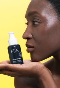 Bottiglia nera con un erogatore bianco, etichettata "CRÈ Recuperami Crema Notturna Restorativa." La mano di una persona tiene il prodotto contro uno sfondo giallo.