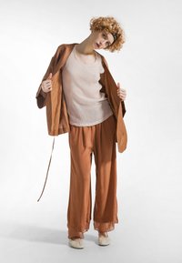 Lekki komplet kimonowy i spodnie w kolorze rdzy, wykonane z miękkiego, płynącego materiału. Góra to beżowa, prążkowana bokserka. Całość dopełniają białe wsuwane buty.