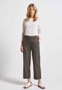 Ljusbeige långärmad tröja i kombination med högmidjade grå rutiga byxor som har sidofickor och tvåknäppning. Krämfärgade sneakers.