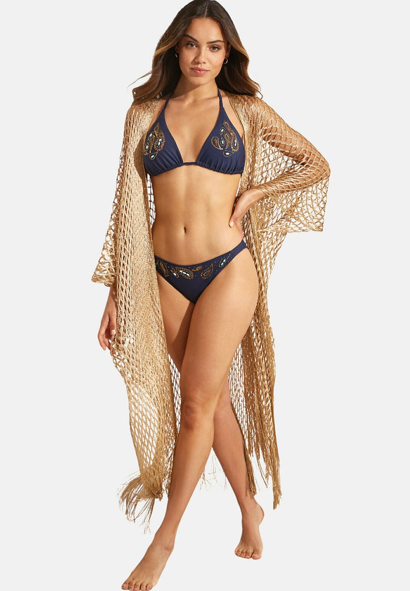 Marine bikini set met versierde details, gecombineerd met een doorschijnende, franjesrijke, gouden haakwerk cover-up, die open geweven en licht van textuur is.