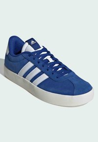 Blå mockaskor med vit tre-stripesdesign, rund tå, platt gummisula och blå textiltunga. Har vita detaljer på hälen.