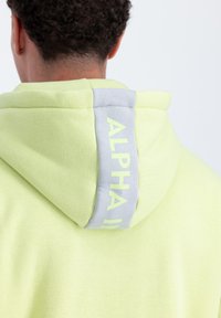 Világoszöld kapucnis felső, hátsó szürke részlettel, melyen világoszöld "ALPHA II" felirat található. Texturált anyag, lazább szabással.