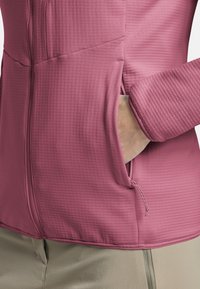 Giacca in pile di colore rosa morbido con un motivo testurizzato, dotata di una cerniera frontale e tasche per le mani sui lati.