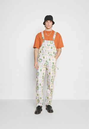 White overalls with colorful square patterns, featuring green leaves and floral designs. Accompanied by an orange T-shirt and black bucket hat.