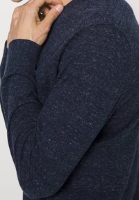 Námořnická dlouhá tričko s texturovaným pletením, se standardním výstřihem a žebrovaným lemem, předvádějící skvrnité detaily po celé látce.