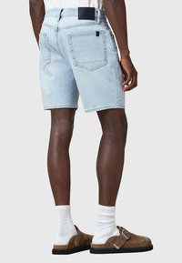 Shorts di denim azzurro con un taglio dritto, cuciture visibili e due tasche posteriori. Indossati con calzini bianchi e sandali marroni.