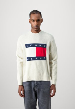 Suéter de mezcla de lana color crema con un gran parche de logo en navy, rojo y blanco que lleva el texto "TOMMY JEANS". Corte holgado con puños y dobladillo de canalé.