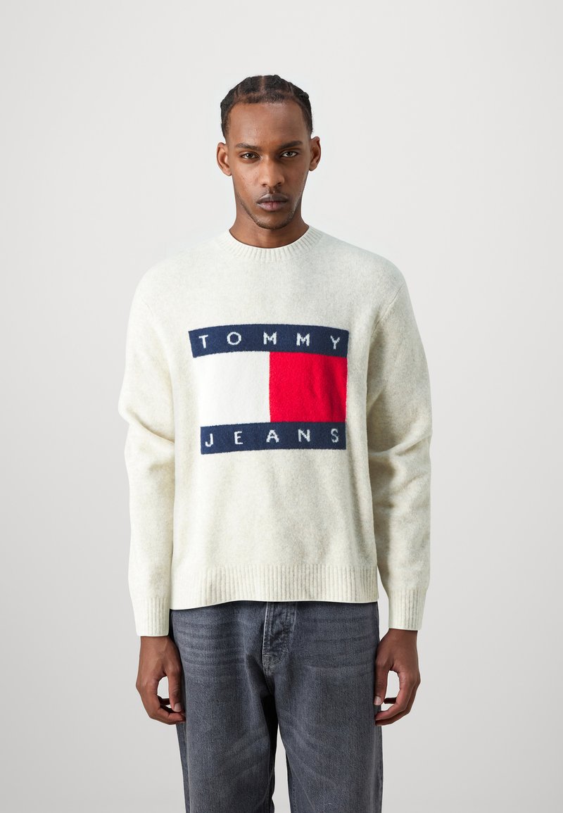 Suéter de mezcla de lana color crema con un gran parche de logo en navy, rojo y blanco que lleva el texto "TOMMY JEANS". Corte holgado con puños y dobladillo de canalé.