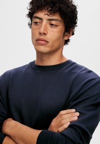 Sudadera azul marino hecha de un tejido suave, con cuello redondo, mangas largas y una textura lisa sin patrones visibles.