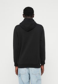 Μαύρο φούτερ με κουκούλα σε χαλαρή γραμμή, με ριμπ μανσέτες και τελείωμα, που διαθέτει λείο ύφασμα. Φορεμένο με ανοιχτόχρωμο μπλε τζιν cargo.