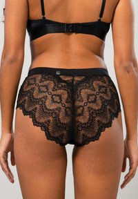 Schwarzes Dessous-Set mit Spitzendetails. Die Unterwäsche hat ein gewelltes Spitzenmuster und einen elastischen Bund. Der BH hat ein breites Band und verstellbare Träger.