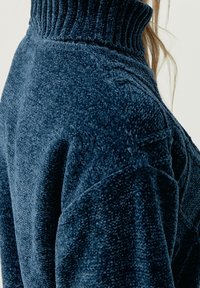 Marinblå fleece-polo med ribbstickad krage och mjuk textur, som har en avslappnad passform och distinkta sömdetaljer på ärmarna.