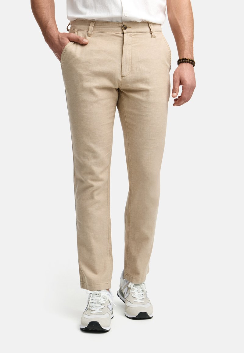 Pantalones de lino beige con corte recto, que cuentan con bolsillos delanteros, cierre de botón y se llevan con zapatillas grises. Textura suave.