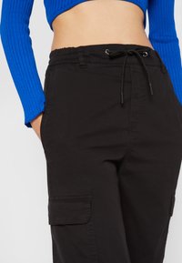 Black cargo pants with an elastic waistband and drawstring. Features side pockets and textured fabric. Paired with a blue ribbed top.