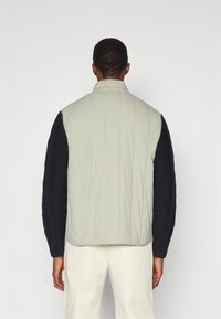 Ανοιχτό πράσινο γεμιστό γιλέκο με ψηλό γιακά και μαύρα πλεκτά μανίκια που διαθέτουν σχέδιο καλωδίου, λεία υφή και πλάγιες τσέπες με φερμουάρ.