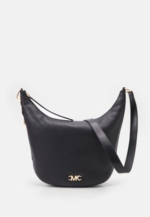 Sac à bandoulière en cuir noir avec logo MK doré, silhouette courbée, bandoulière réglable et fermeture éclair sur fond clair.