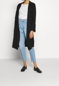 Czarny długi płaszcz, biały top z detalami z oczek, jasnoniebieskie dżinsy i czarne mokasyny. Charakteryzuje się luźnym krojem i zwiewną sylwetką.