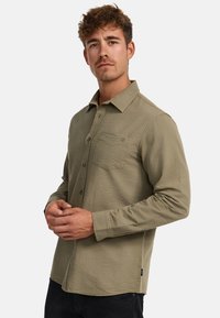 Olivegrünes langärmliges Hemd aus strukturiertem Stoff, mit Button-Down-Kragen, einer einzelnen Brusttasche und schwarzen Akzenten am Saum.
