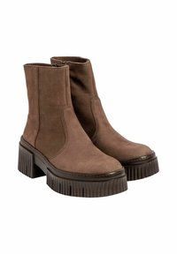 Botas de tobillo de ante marrón con suelas ridged gruesas y tacones cuadrados, que presentan cremalleras laterales y detalles de costura sobre un fondo blanco.