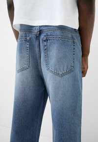 Jeans de mezclilla en azul claro, con una textura suave, diseño clásico de cinco bolsillos y costuras contrastantes a lo largo de los bolsillos y las costuras.