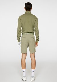 Golfasusteet, joissa on pitkähihaista oliivinvihreää paitaa ja siihen sopivat shortsit, molemmat hengittävästä kankaasta. Mukana tulee myös hansikas ja valkoiset sukat logolla.