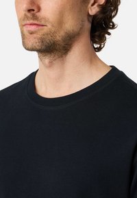 Black cotton crew neck sweatshirt with a smooth texture, plain design, and contrasting stitching along the neck and shoulder seams.