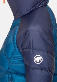 Giacca imbottita blu e blu navy con un design trapuntato, caratterizzata da un logo di un mammut sulla manica e un cappuccio regolabile.