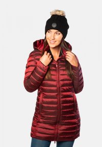 Manteau rembourré rouge avec des coutures horizontales, fermeture éclair à l'avant et capuche. Bonnet en tricot noir texturé avec pompon en fausse fourrure.