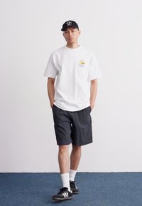 Hvit bomulls t-skjorte med grafikk, parret med mørke mønstrede shorts. Svarte caps og svarte sneakers med hvite striper fullfører antrekket.