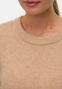 Beige Strickpullover mit einem gerippten Rundhalsausschnitt. Weiche Textur mit leicht flauschigem Aussehen. Nahaufnahme des Kragenbereichs und der Haut.