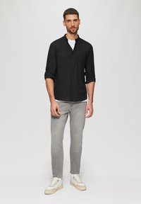 Chemise noire à manches longues avec col montant, associée à un jean gris clair et des baskets blanches avec des accents crème. Coupe décontractée avec les manches retroussées.