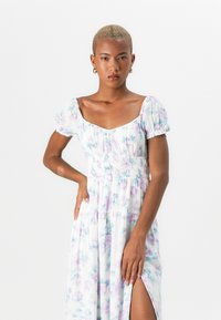 Rochie maxi florală din țesătură ușoară, cu talie elastică, mâneci bufante și un slit lateral, având o paletă de culori pastelate de violet și albastru.