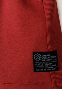 Tissu de sport rouge avec une section texturée à côtes et une étiquette noire avec du texte blanc indiquant la marque et l'utilisation.