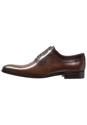 Chaussure habillée Oxford pour homme en cuir marron, avec détails à brogue et laçage fermé sur un petit talon empilé, sur fond blanc.