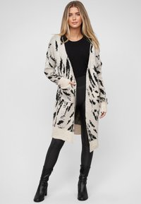 Sweter kardigan w kolorze kości słoniowej z czarnym wzorem w zwierzęta, posiadający długie rękawy, dwie przednie kieszenie oraz otwarty krój.