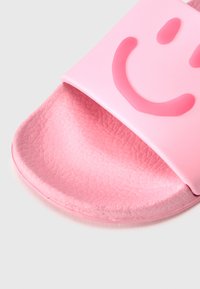 Ροζ σαγιονάρα από καουτσούκ με υφή στο πέλμα και φαρδιά λουρί που διαθέτει ανάγλυφο σχέδιο με χαμογελαστό πρόσωπο. Ομοιόμορφη, λεία επιφάνεια.