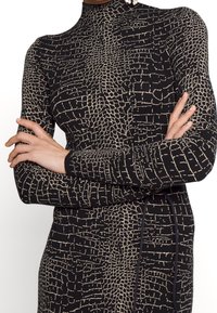 Robe noire près du corps avec un motif unique en crocodile beige, col haut et manches longues en tissu texturé avec des détails sur les côtés.