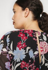 Vestido preto com flores vermelhas e azuis. Apresenta uma abertura nas costas em forma de buraco de chave e uma textura leve e transparente.